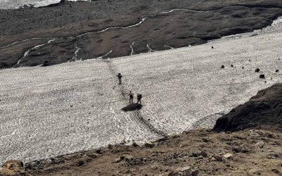 Hikers trekking across a glacier in Iceland with rugged volcanic terrain.