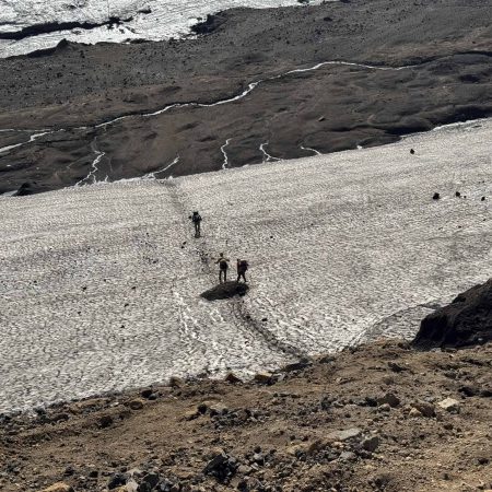 Hikers trekking across a glacier in Iceland with rugged volcanic terrain.