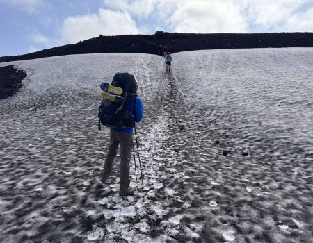 Hiker trekking on icy glacier with backpack and trekking poles in Iceland.