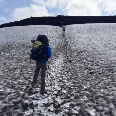 Hiker trekking on icy glacier with backpack and trekking poles in Iceland.