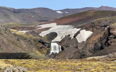 Scenic Icelandic glacier landscape with waterfall and snow patches.
