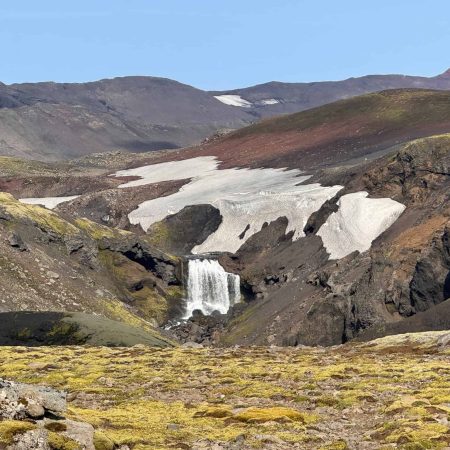 Scenic Icelandic glacier landscape with waterfall and snow patches.