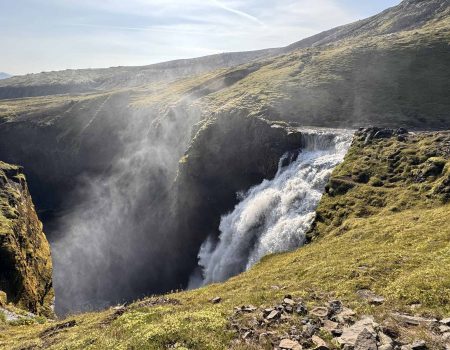 Scenic Icelandic waterfall cascading into a deep canyon with lush green surroundings.