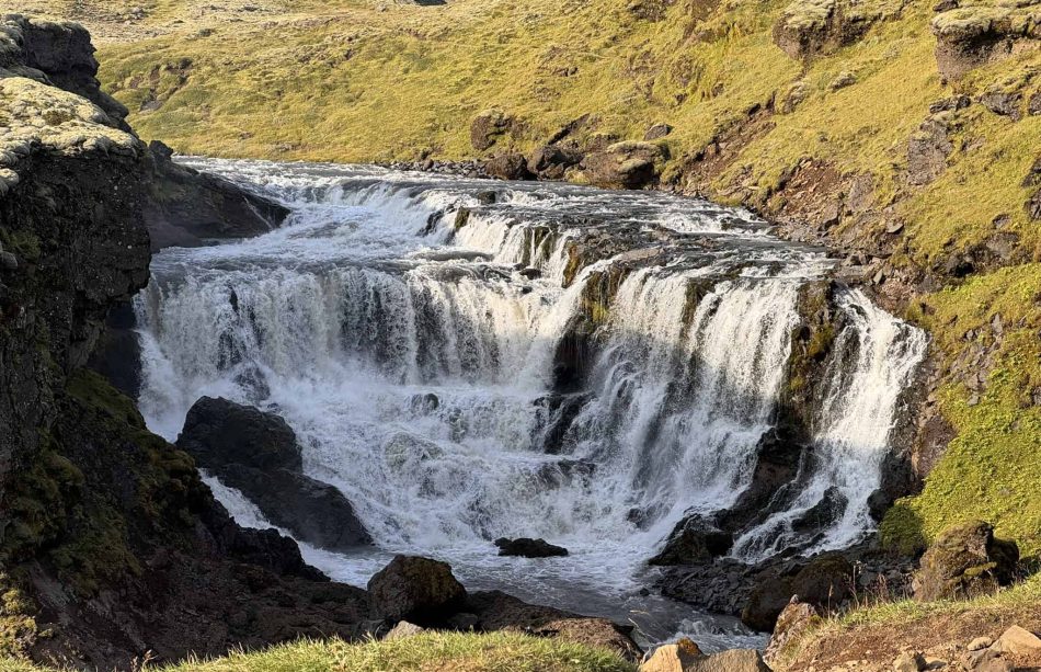 Scenic Iceland waterfall with lush green surroundings and flowing water.