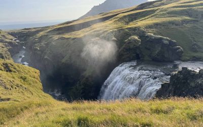 Scenic Icelandic waterfall with lush green hills and mountain backdrop.